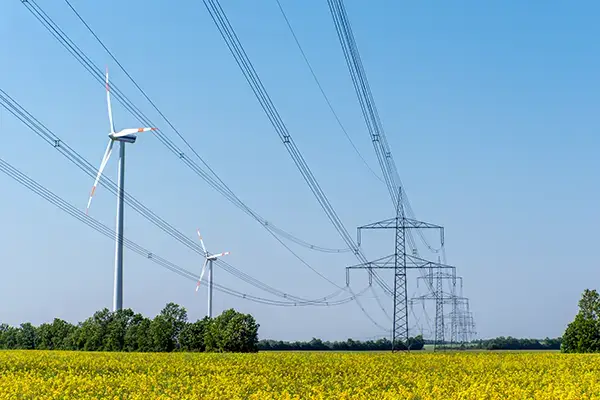 High-voltage power transmission lines and wind turbines generating renewable energy in an open field.
